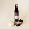 ail et olives 3 Bouteille de vinaigre balsamique ail et olive noire posée sur des rondins de bois, accompagnée d’une gousse d’ail et de plusieurs olives noires