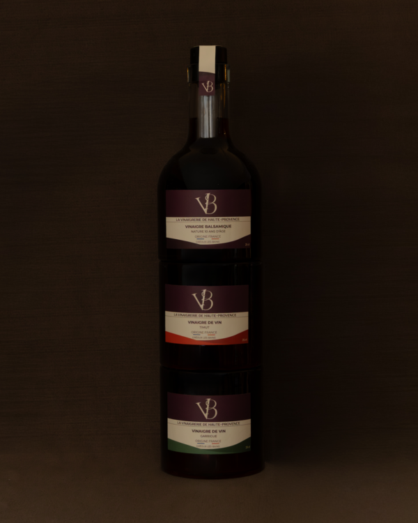 Trois bouteilles empilables de vinaigre artisanal de la Vinaigrerie de Haute-Provence, comprenant un balsamique 10 ans, un vinaigre de vin timut et un vinaigre de vin garrigue