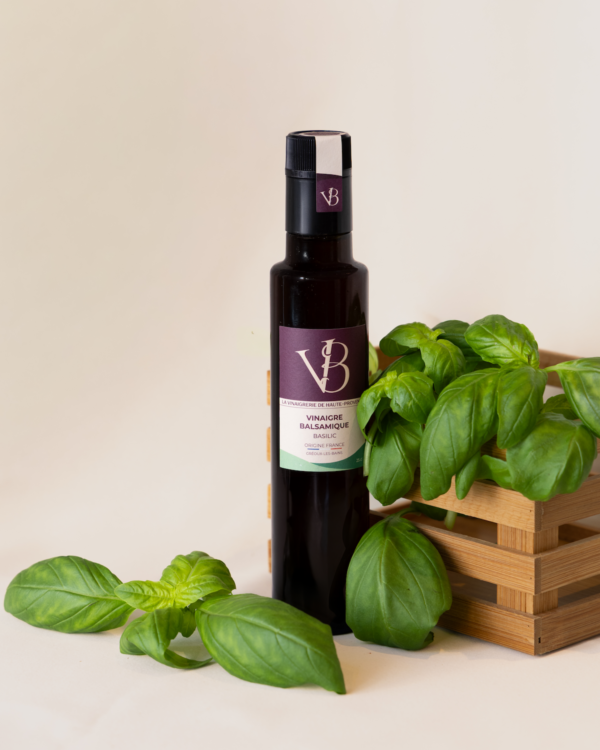 Bouteille de vinaigre balsamique au basilic posée à côté d’un panier en bois rempli de feuilles de basilic fraîches