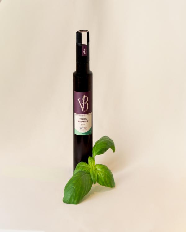 Bouteille de vinaigre balsamique au basilic accompagnée de feuilles de basilic frais sur fond clair