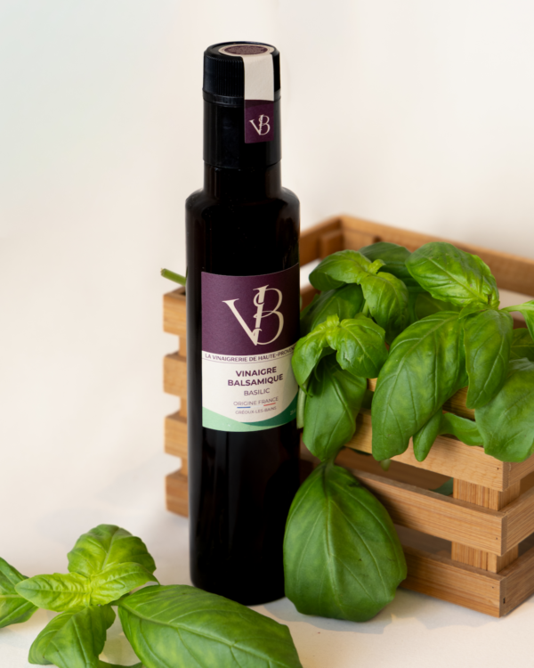 Bouteille de vinaigre balsamique au basilic posée à côté d’un panier en bois rempli de feuilles de basilic fraîches