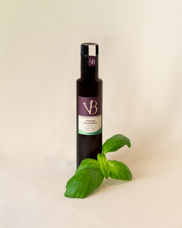 Bouteille de vinaigre balsamique au basilic accompagnée de feuilles de basilic frais sur fond clair