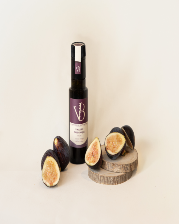 Bouteille de vinaigre balsamique à la figue entourée de figues fraîches coupées, posées sur des rondins de bois