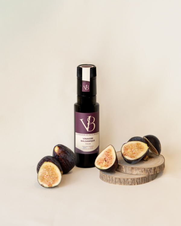Bouteille de vinaigre balsamique à la figue entourée de figues fraîches coupées, posées sur des rondins de bois