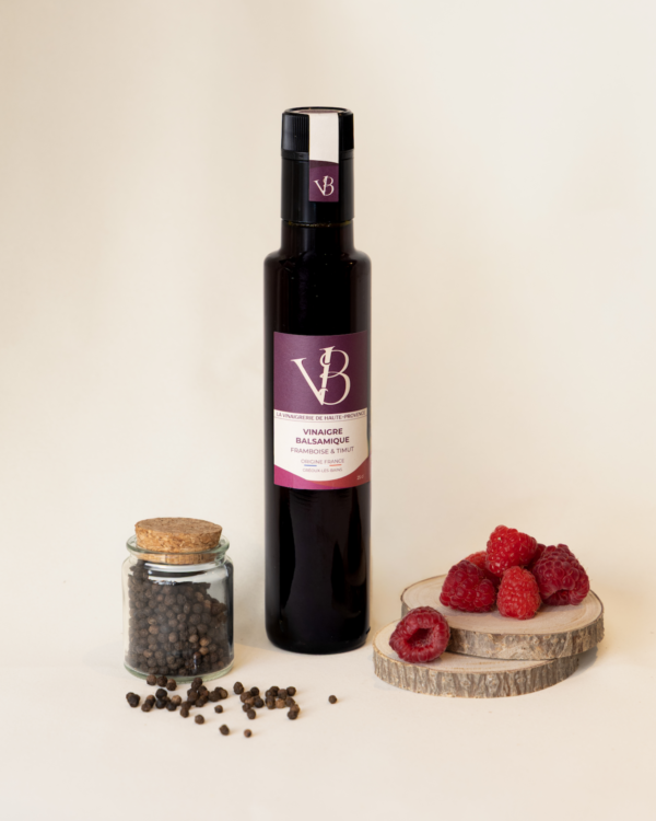 framboise 3 Bouteille de vinaigre balsamique framboise & timut entourée de framboises fraîches et d’un pot de poivre