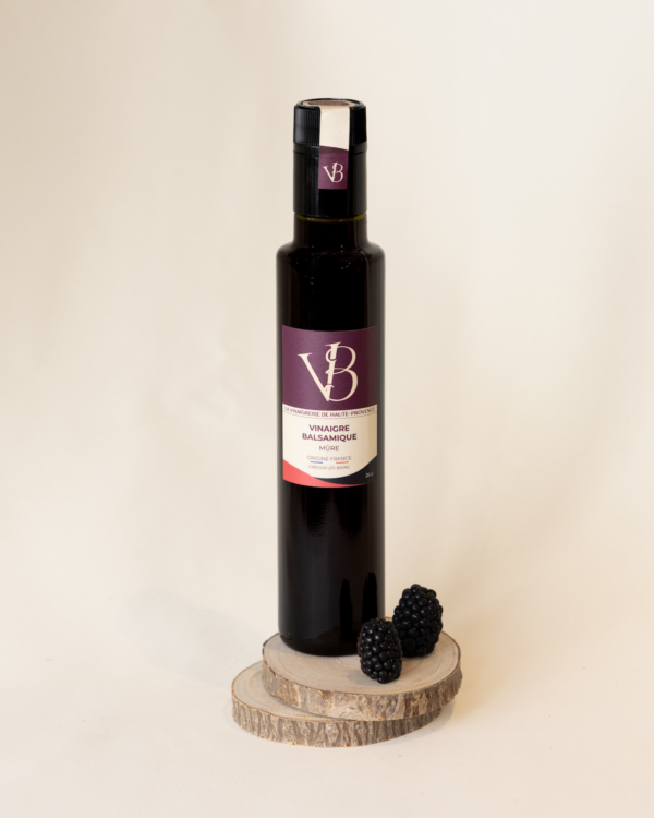 Bouteille de vinaigre balsamique à la mûre avec deux mûres fraîches sur fond beige