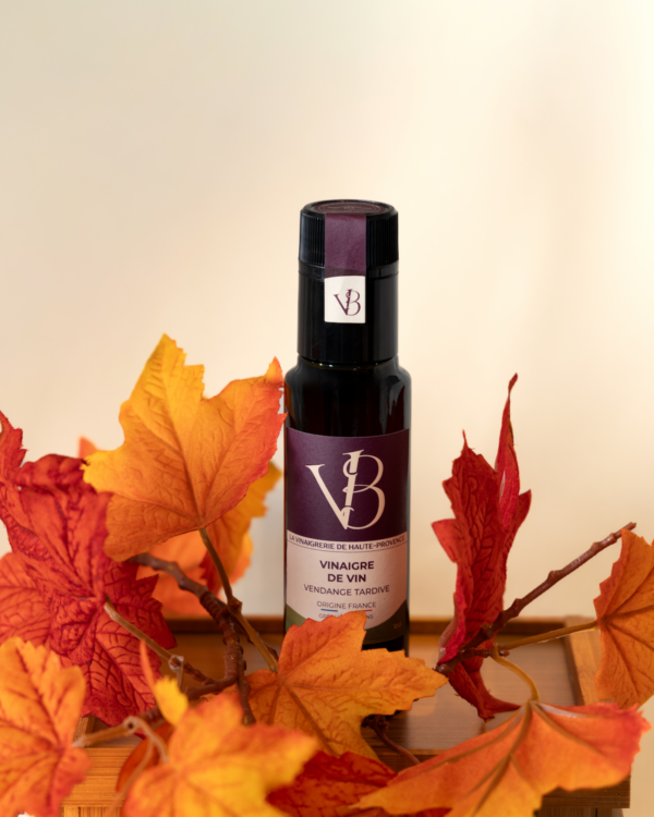 Bouteille de vinaigre de vin vendange tardive entourée de feuilles d’automne rouges et orangées