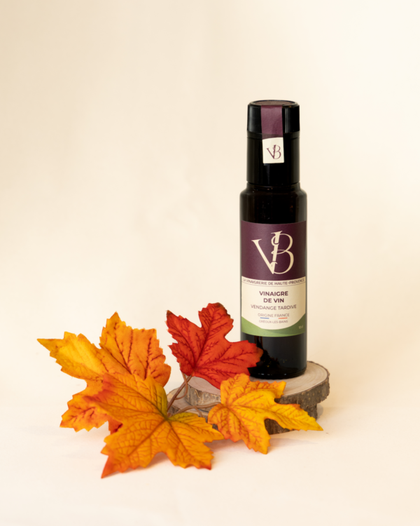 Bouteille de vinaigre de vin vendange tardive posée devant des feuilles d’automne orangées