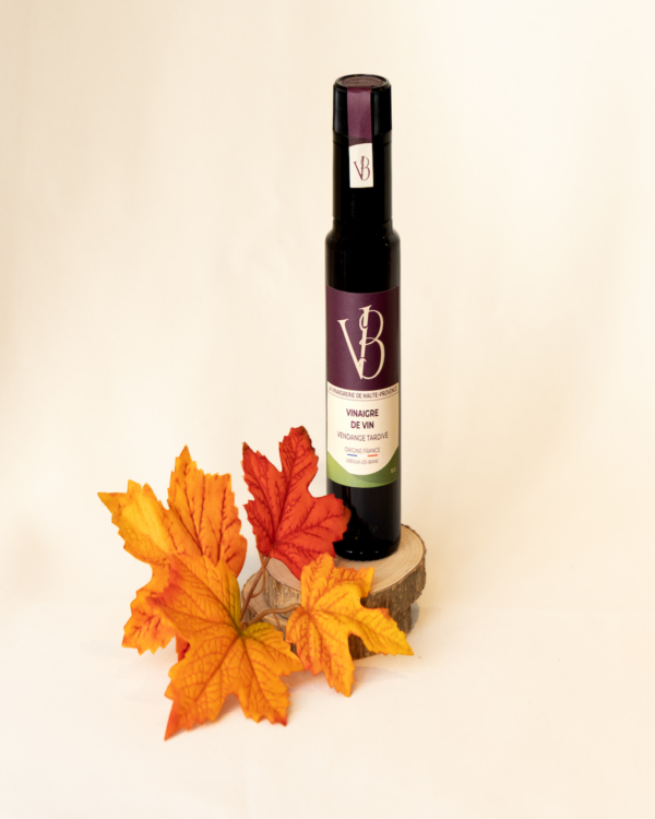 Bouteille de vinaigre de vin vendange tardive posée devant des feuilles d’automne orangées