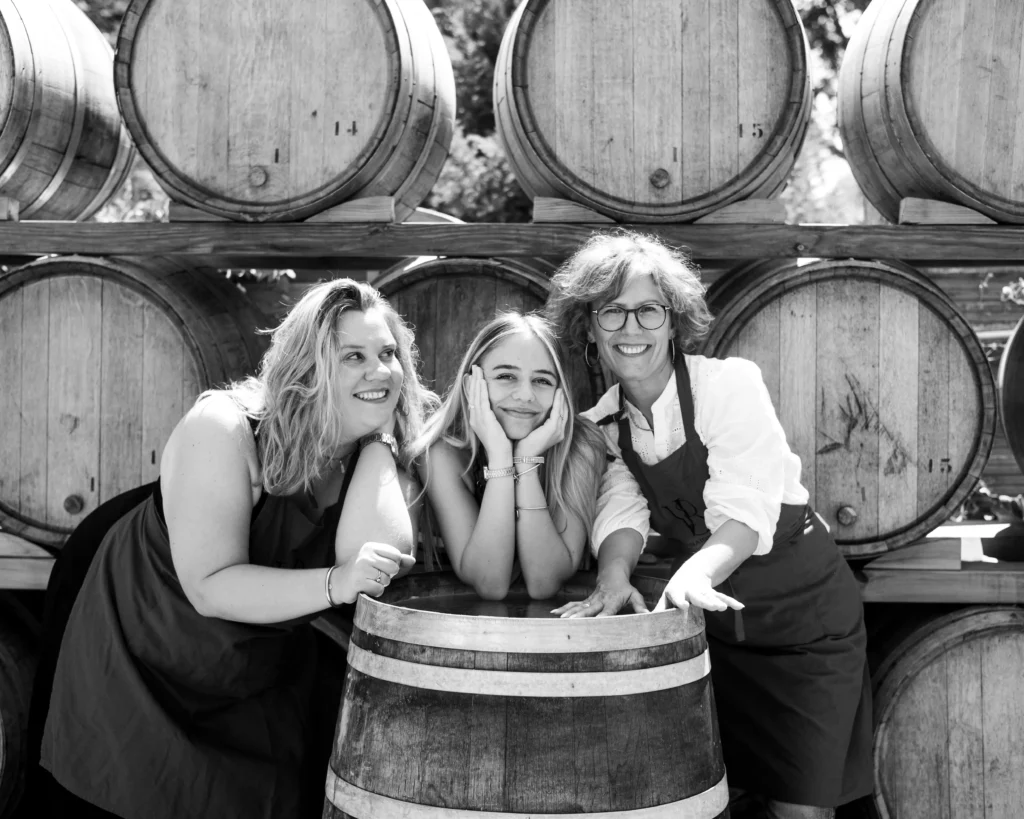 Trois femmes souriantes posent devant des fûts en bois à la Vinaigrerie de Haute-Provence