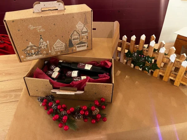 Coffret de Noël artisanal contenant des bouteilles de vinaigre et balsamique, présenté sur une table avec une décoration festive en bois et baies rouges.